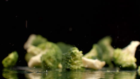 Frischer-Grüner-Brokkoli-Fällt-In-Zeitlupe-Auf-Ein-Glas-Mit-Spritzern-Und-Wassertropfen
